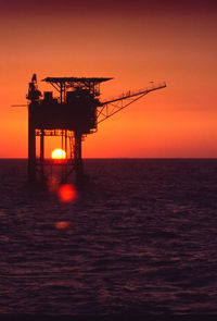 Silhouette built structure on sea against orange sky