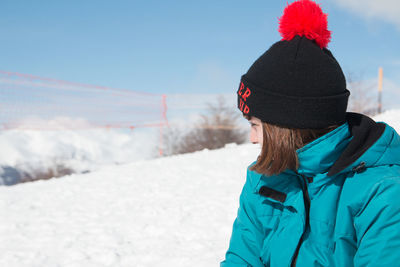 Young woman wearing hat sitting against snow covered landscape