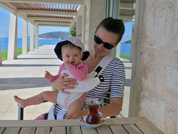 Smiling woman holding daughter while sitting by turkish tea on table