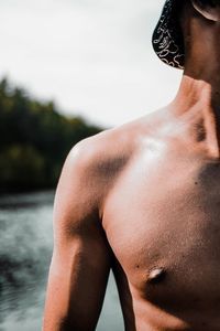 Midsection of shirtless man standing in water against sky