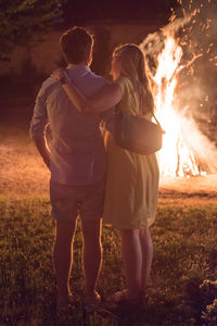 Rear view of couple standing on field by campfire