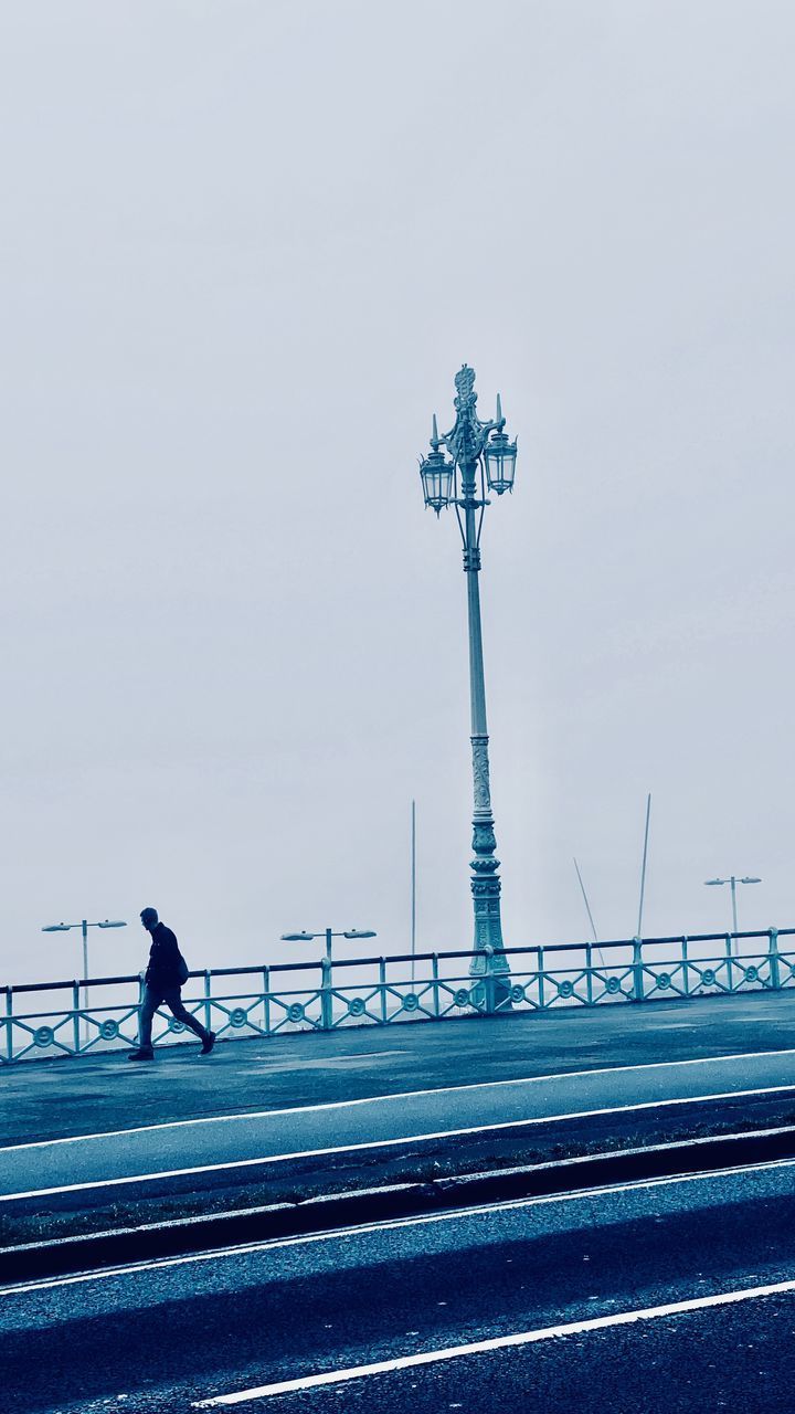 MAN WALKING ON STREET AGAINST SKY