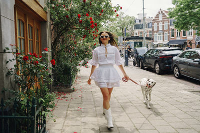 Portrait of young woman with dog standing on footpath