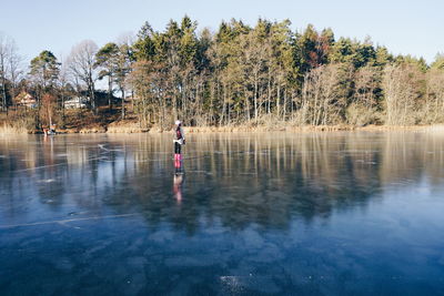 Mid distant view of woman standing on frozen lake against trees