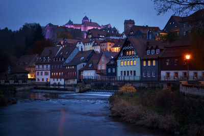 Illuminated buildings by street against sky at dusk