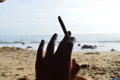 Close-up of hand against sea against sky