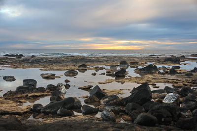 Rocks on beach against sky during sunset