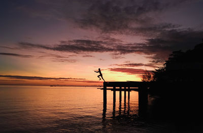 Silhouette man in sea against sky during sunset