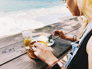 Midsection of woman holding drink at sea shore