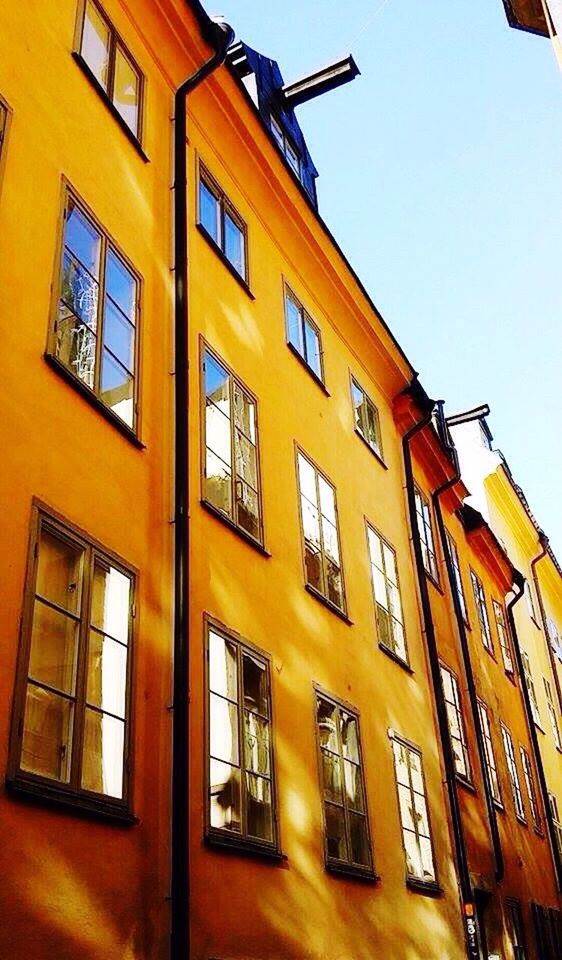 window, building exterior, architecture, built structure, low angle view, clear sky, city, residential building, glass - material, building, yellow, balcony, day, repetition, building story, sky, blue, in a row, apartment, outdoors, city life, office building, no people, tall