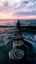 Scenic view of wooden posts leading out to sea against sky during sunset