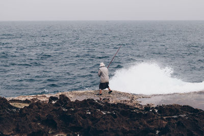 Full length of man fishing in sea against sky