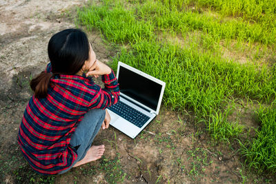 Rear view of woman crouching by laptop on field