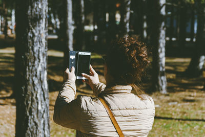 Rear view of woman photographing with mobile phone in forest