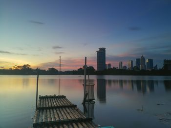 Scenic view of lake by buildings against sky during sunset