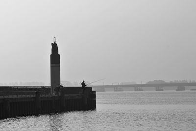 Man fishing by lighthouse against clear sky