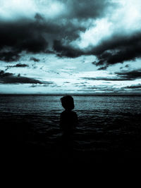 Silhouette of people standing on beach against cloudy sky