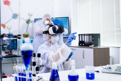 Scientist wearing virtual reality simulator colleague in background at laboratory