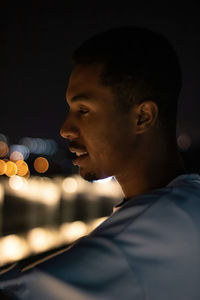 Side view of man looking away while standing outdoors at night