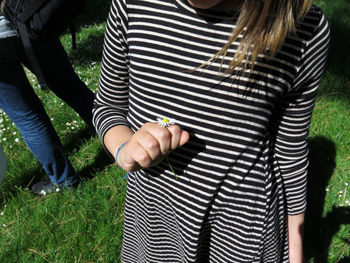 Midsection of girl holding flower while standing on field during sunny day