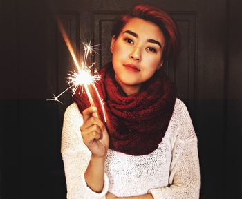 Portrait of woman holding sparkler while standing against wall