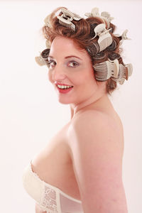 Portrait of smiling young woman with hair curlers against white background