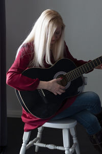 Beautiful young blonde woman in a red dress with a black guitar, favorite hobby