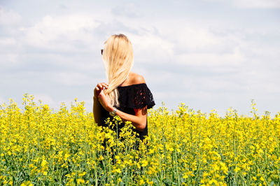 Young woman with hand in hair standing on oilseed rape field