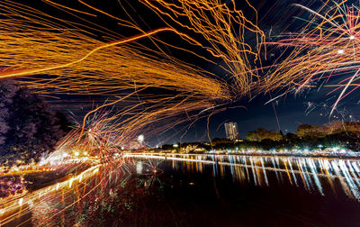 Light trails over river against sky at night