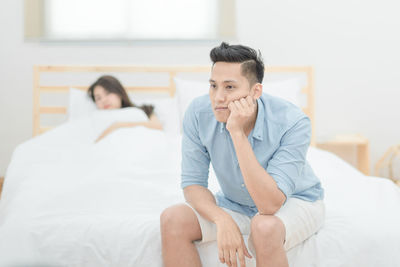 Young man sitting on bed at home