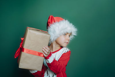 Happy smiling caucasian boy in santa tee shirt and hat holding a box with christmas present