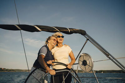 Cheerful female friends looking away while standing in boat against sky