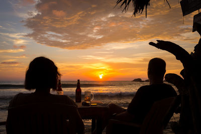 Silhouette people sitting on beach during sunset