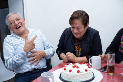 An older man with his friends celebrating his birthday, laughing at an indoor party.