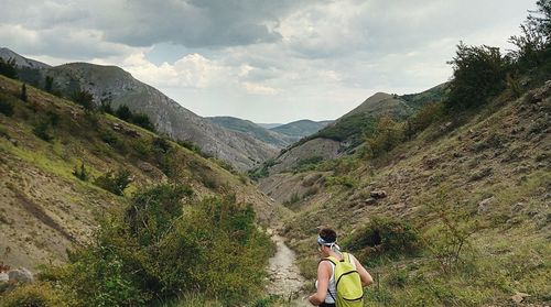 Rear view of young woman with backpack walking on mountain against cloudy sky