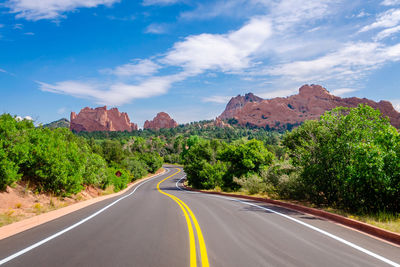 Road amidst trees and mountains against sky