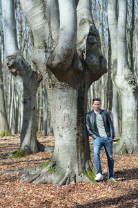 Portrait of young man standing by tree trunk