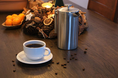 White porcelain cup of coffee and stainless steel french press on festively decorated wood table