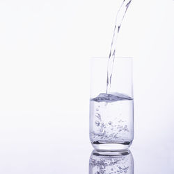 Close-up of glass pouring water against white background