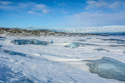 Mid distance view of person standing on snow covered mountain against blue sky