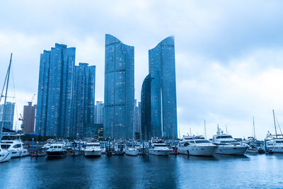 Sailboats in city by sea against sky