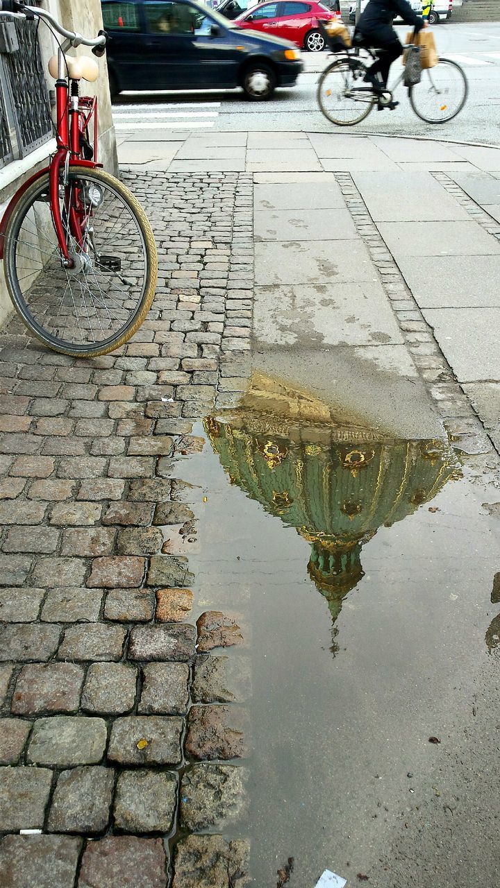 transportation, street, mode of transport, land vehicle, bicycle, high angle view, road, paving stone, cobblestone, city, car, puddle, road marking, water, parking, city life, stationary, travel, sidewalk