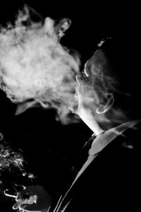 Close-up of man smoking cigarette against black background