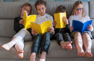 Four children sitting comfortably together on sofa in living room and doing prep work for school