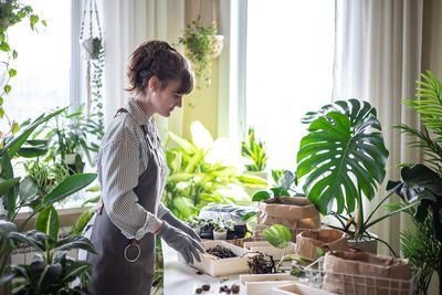 Side view of woman holding potted plant at home