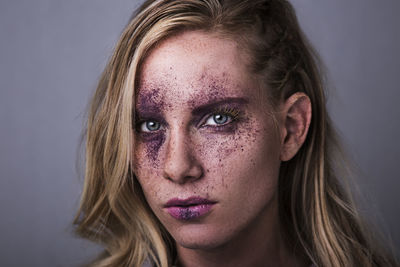 Close-up portrait of woman with purple bruise make-up against gray background