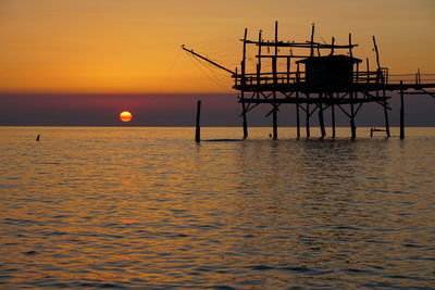 Silhouette built structure over sea against sky during sunset