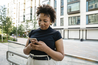 Happy businesswoman using smart phone in front of railing