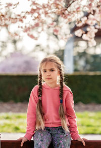 Portrait of cute serious little girl with pensive look in spring park outdoors looking at camera