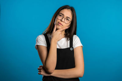 Portrait of young woman standing against blue background